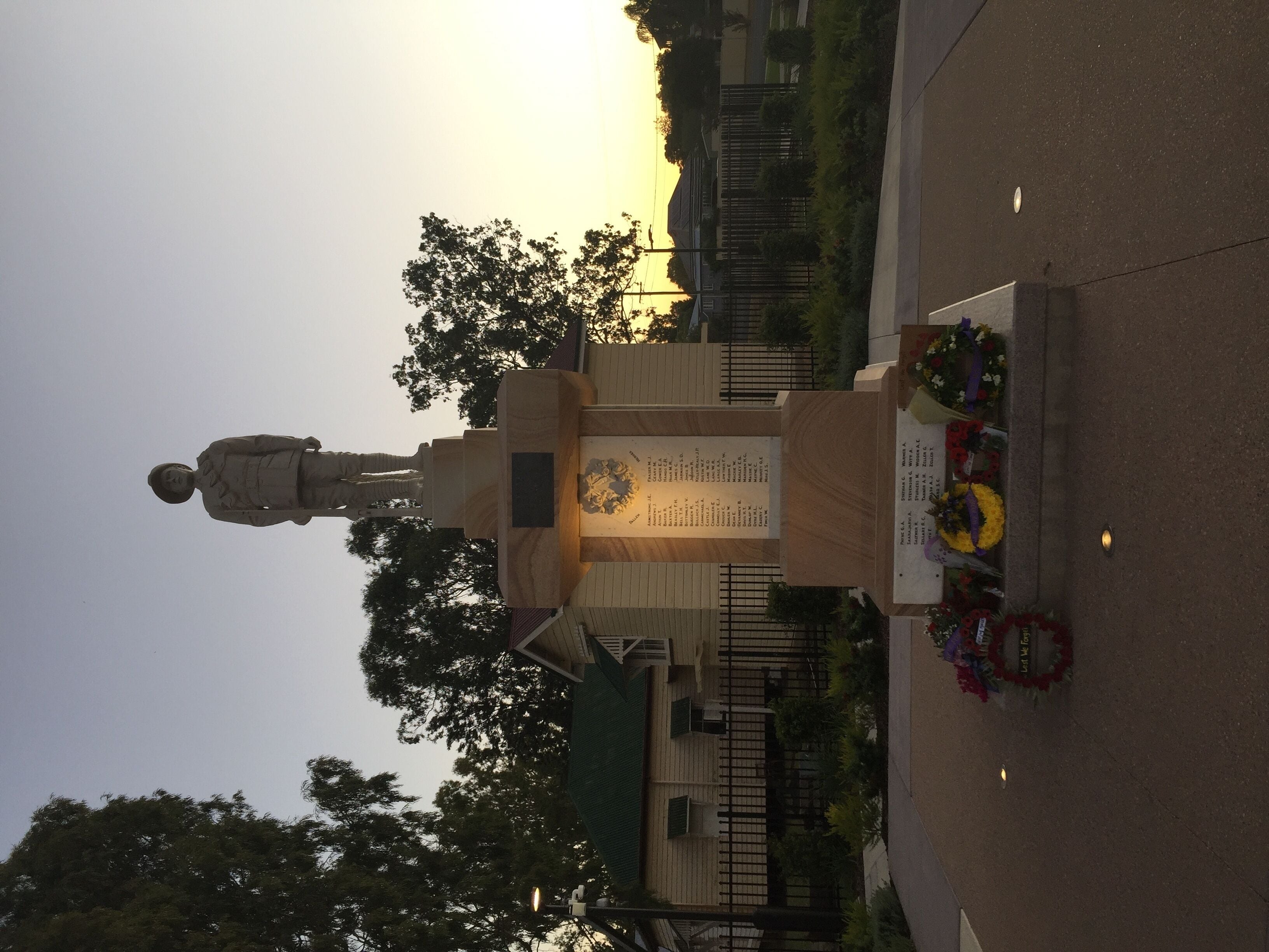 A statue in a public square with a plaque and flowers.