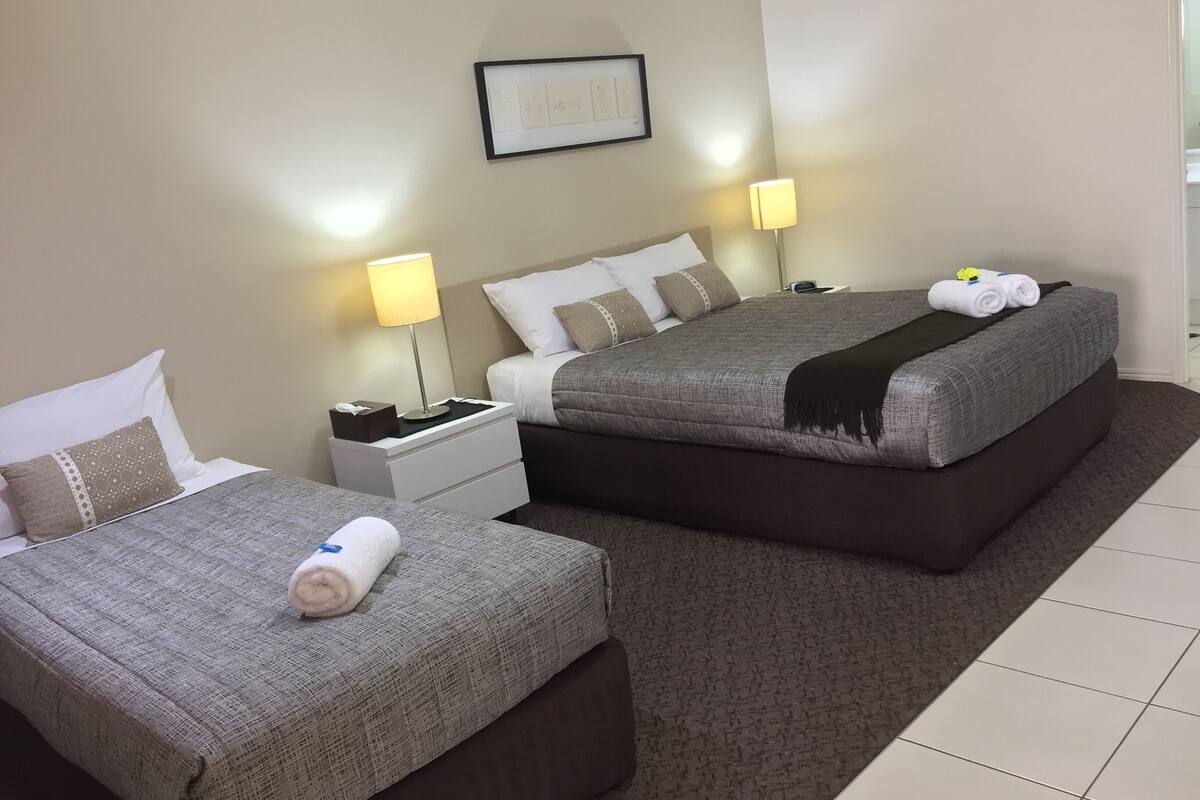 A hotel room with two beds, a nightstand, a lamp, and a framed picture on the wall.