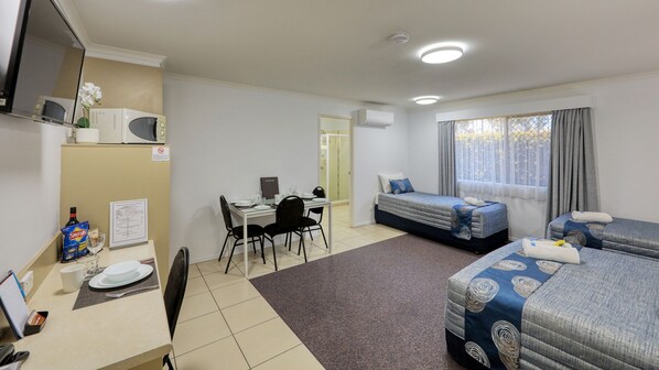A hotel room with a bed, a desk with a chair, a small table with a chair, a TV, and a window with curtains.