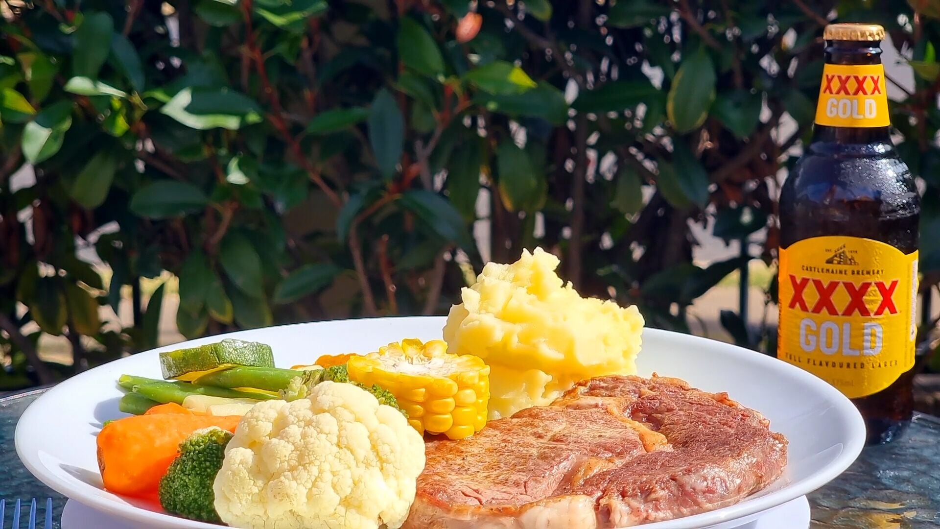 En tallerken mad med bøf, mos kartofler, majs, broccoli og gulerødder, samt en flaske XXXX Gold øl.