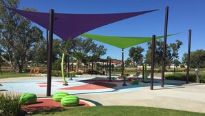 Un parque infantil con juegos de colores y zonas con sombra.