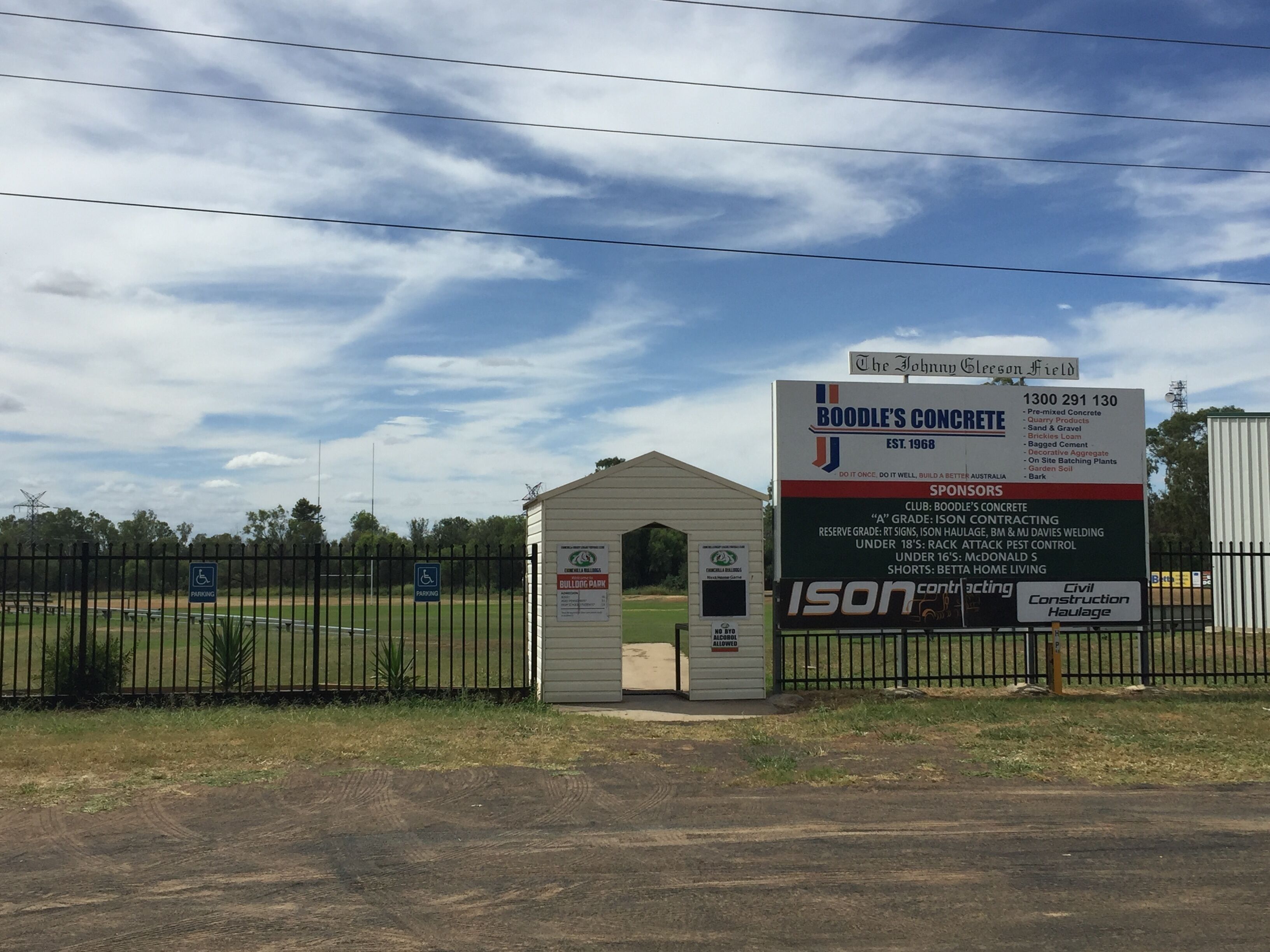 A construction site with a sign for Boodle's Concrete, a small shed, and a fenced area with handicap parking signs.