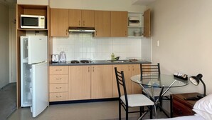 A compact kitchen with wooden cabinets, a microwave, a refrigerator, a toaster, and a glass table with chairs. - Atelier Serviced Apartments (Newtown)