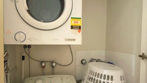 A front-loading washing machine and a dryer stacked on top of each other, with a laundry basket to the right. - Atelier Serviced Apartments (Newtown)