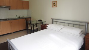 A compact hotel room with a bed, a small table, and a kitchenette. - Atelier Serviced Apartments (Newtown)