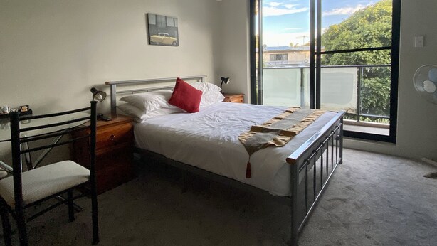A bedroom with a bed, a chair, a bedside table, a window with a view of greenery, and a painting on the wall. - Atelier Serviced Apartments (Newtown)