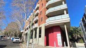 A multi-story building with a red entrance door, numbered 130, and a clear blue sky. - Atelier Serviced Apartments (Newtown)