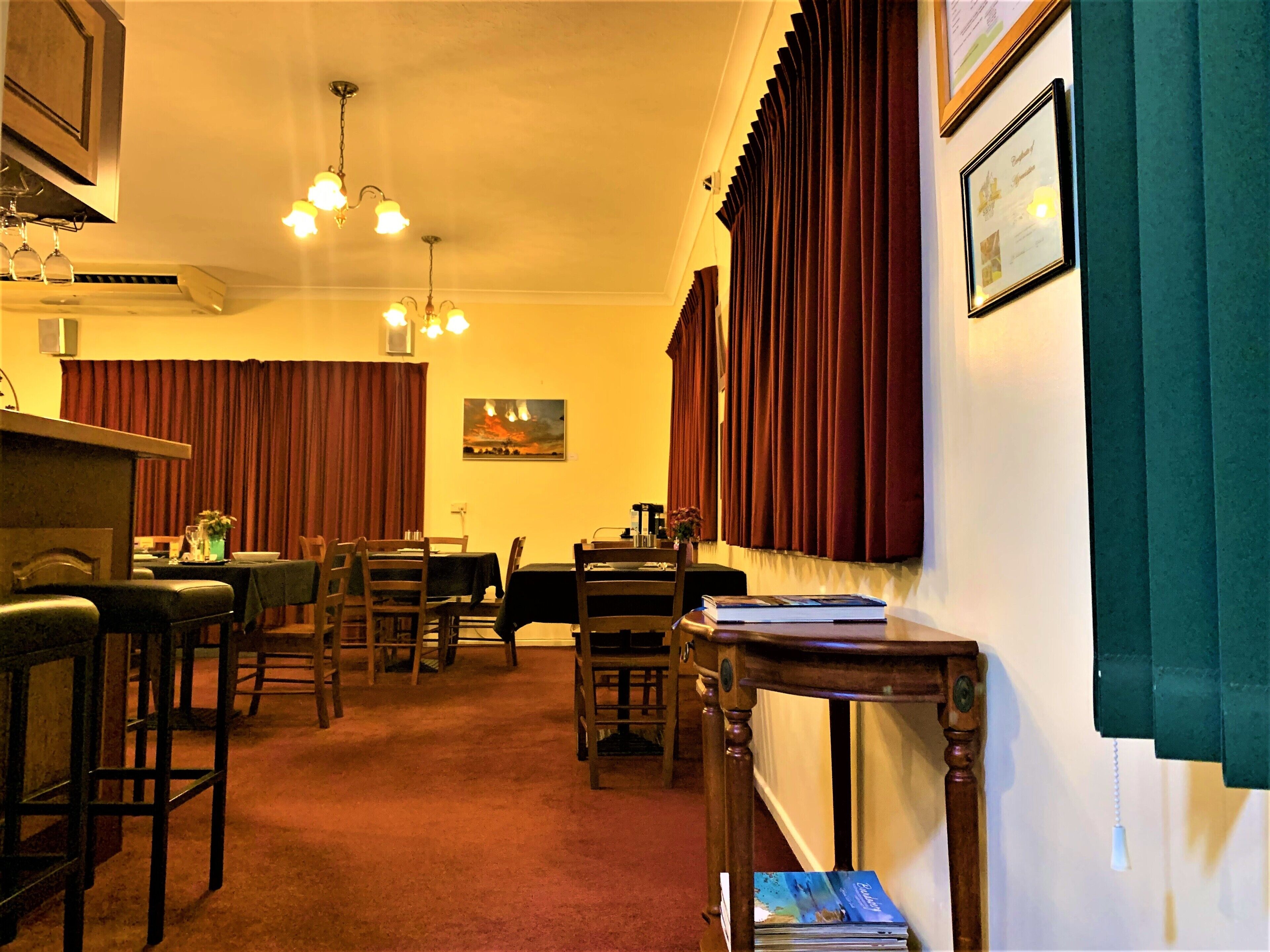 Ein gemütlicher Essbereich mit Holzsesseln und -tischen, eine Bar mit Hockern und ein Gemälde an der Wand.