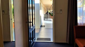 Un pasillo de hotel con una puerta que da a una habitación, una silla y un ventanal con cortinas.