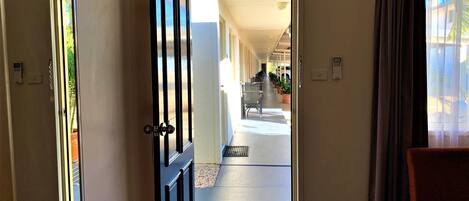 A hotel corridor with a door leading to a room, a chair, and a window with curtains.
