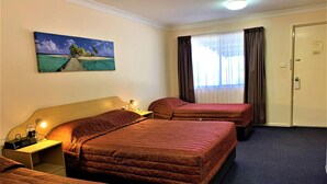 Habitación de hotel con dos camas, un cuadro de una playa, un escritorio con lámpara y una puerta con un cartel.