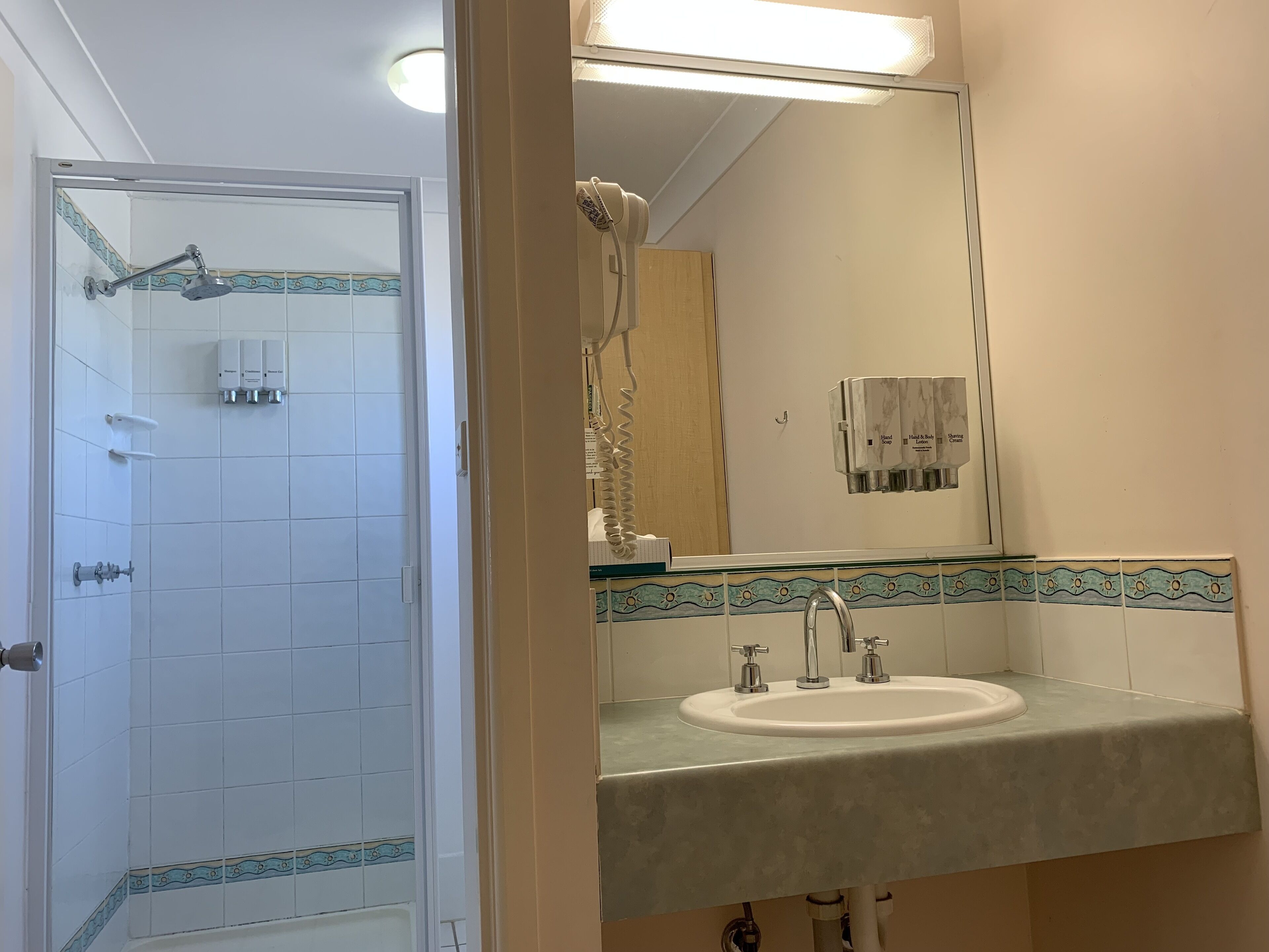Um banheiro com box de vidro, pia com bancada de mármore e espelho com moldura de azulejos decorativos.