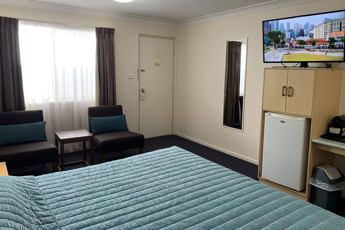 A hotel room with a bed, a desk, a chair, a television, and a refrigerator.