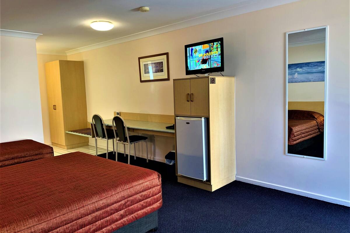 A hotel room with two beds, a small kitchenette, a television, and a framed picture on the wall.