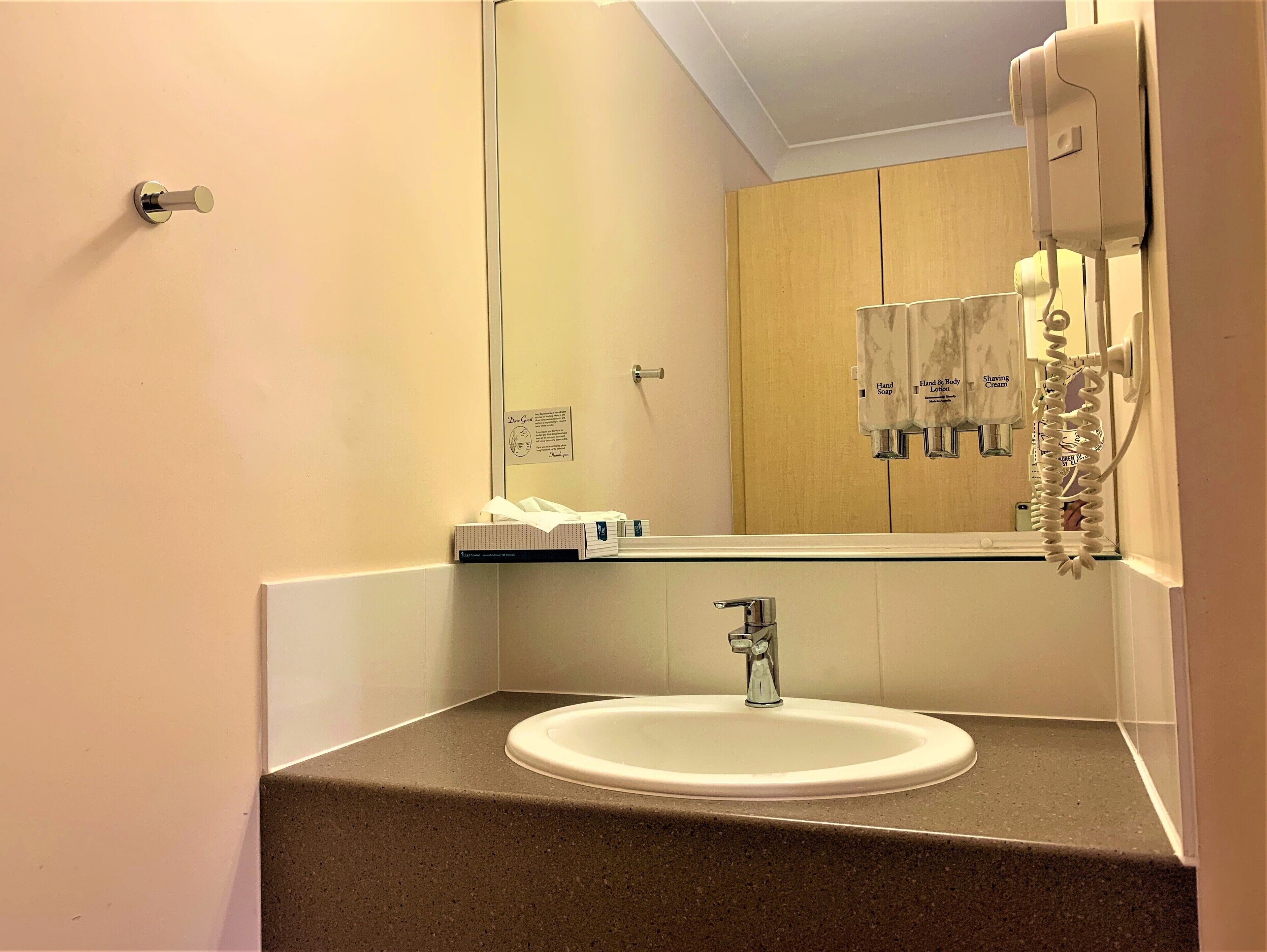 A bathroom with a sink, mirror, and hand soap dispenser.