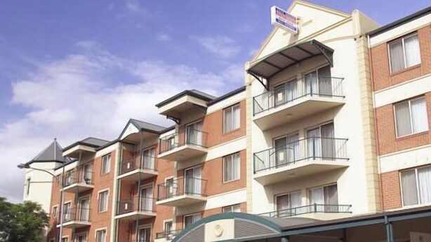 Un edificio de apartamentos con varios pisos, balcones, un acceso cubierto y una señal que indica que es una propiedad de alquiler.