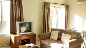Una sala de estar con un sofá, un televisor sobre un mueble de madera, una mesita y cortinas en las ventanas.