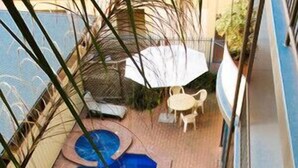 Una piscina pequeña al aire libre con borde de ladrillo, rodeada por una cerca de metal y una pequeña mesa con sillas.