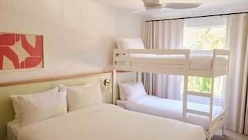 Une chambre avec un lit superposé, un lit simple, un ventilateur de plafond et une fenêtre avec des rideaux.