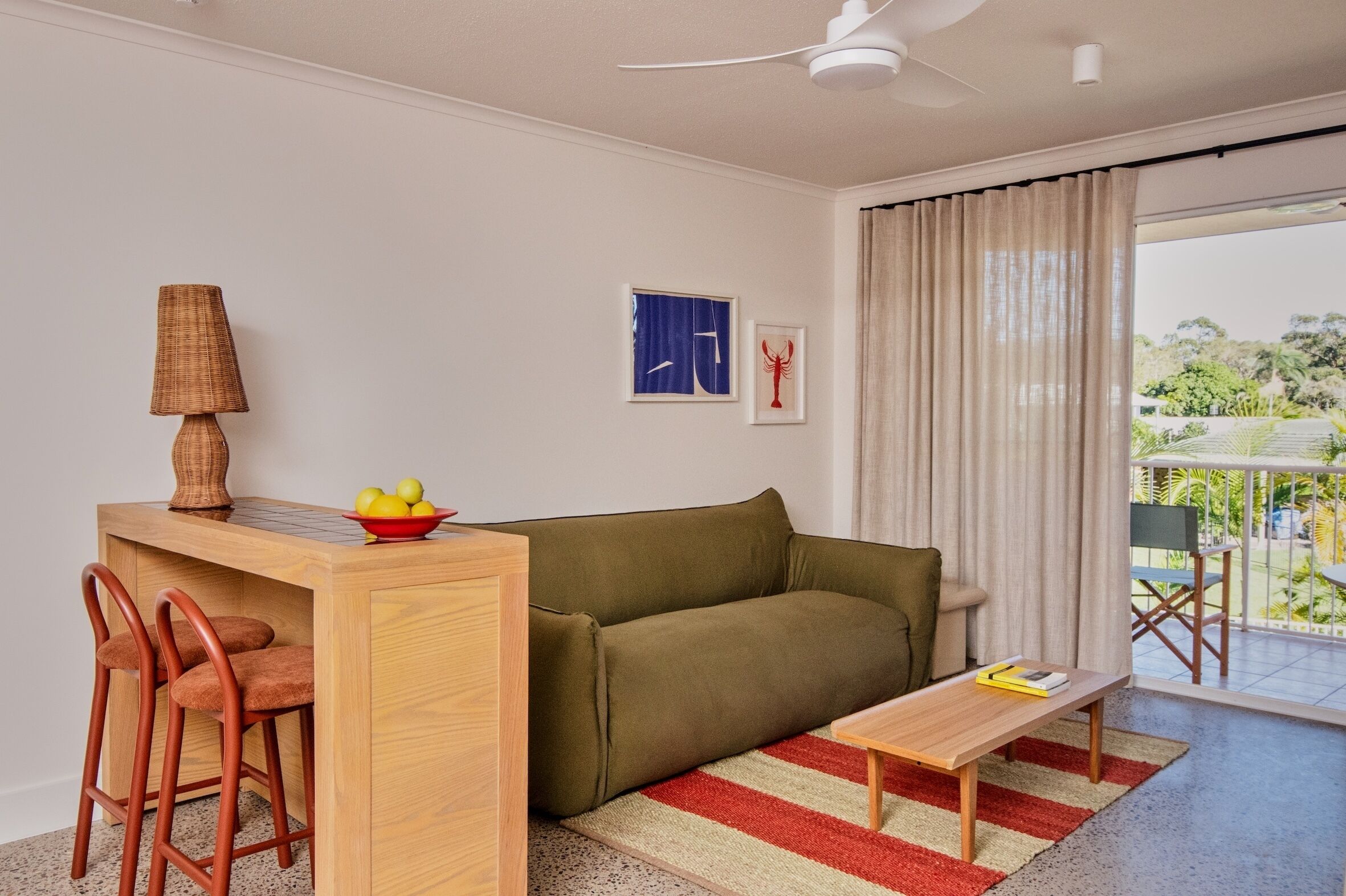Un espace de vie compact comprenant un canapé, une petite table, un coin repas avec des chaises, un ventilateur de plafond et une vue sur l’extérieur.