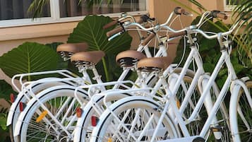 Une rangée de vélos blancs est garée devant un bâtiment, avec de grandes feuilles vertes et une fenêtre en arrière-plan.