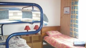 Una stanza con letti a castello, un letto singolo, un armadio in legno e una finestra con tende.