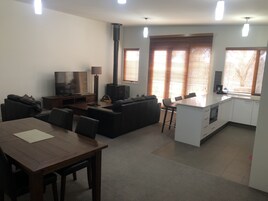 Una sala moderna con un sofá, televisor y mesa de comedor. Se observa una cocina con estufa y alacenas.