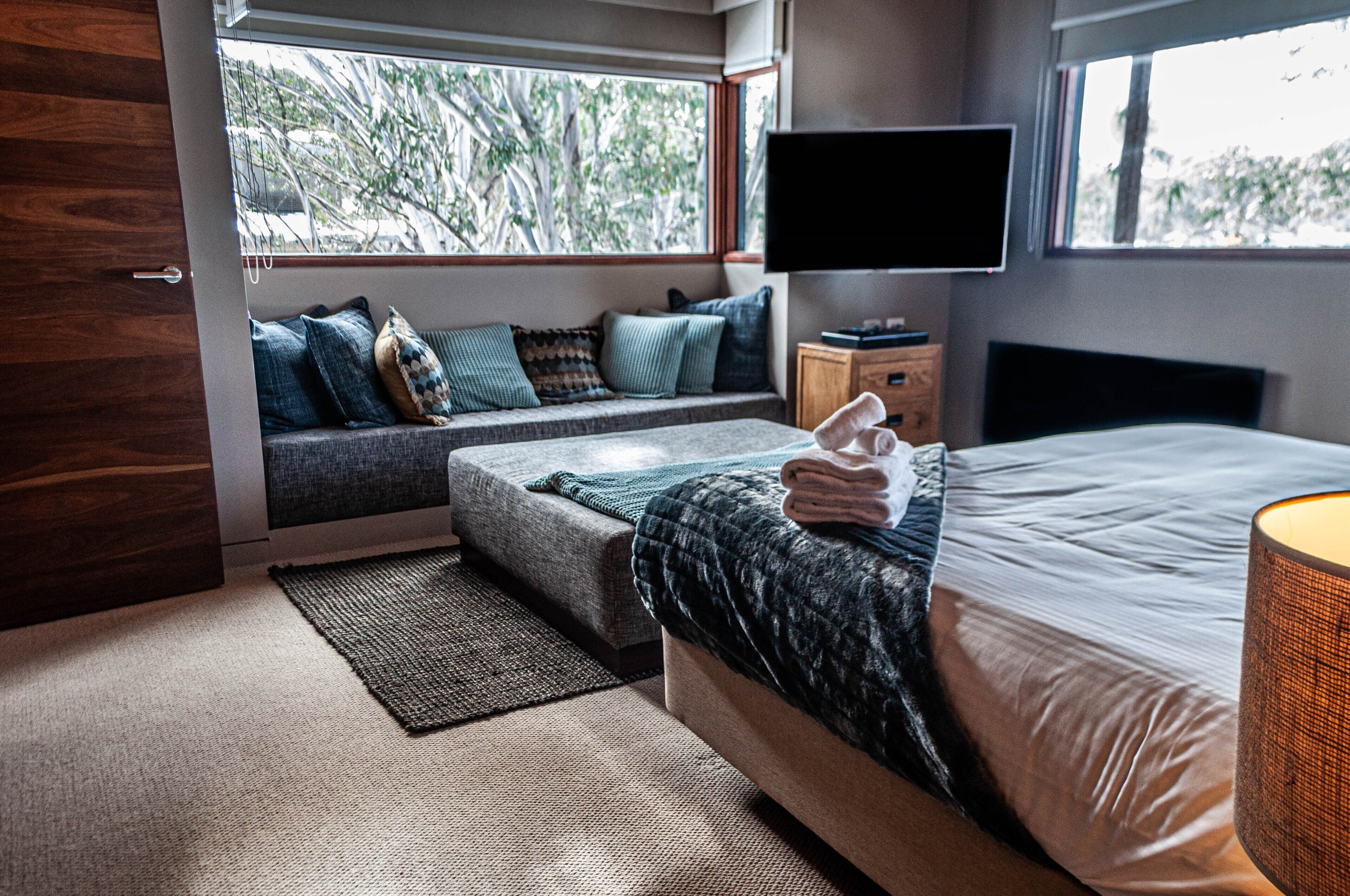 A bedroom with a bed, a TV, a window, a sofa, and a nightstand.