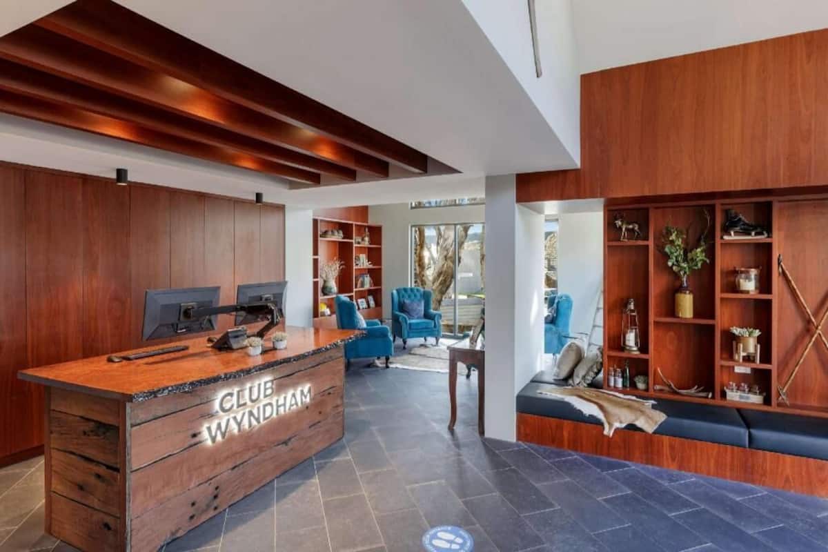 A modern reception desk with 'CLUB WYNDHAM' signage, a seating area with blue chairs, and a wooden bookshelf.