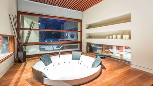 A modern bathroom with a round sink, wooden slatted ceiling, large window, and built-in shelves.