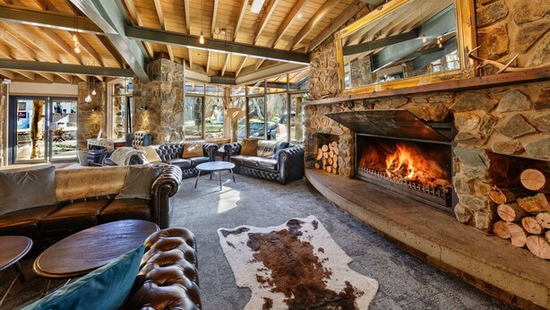 A cozy lounge area with leather sofas, a stone fireplace, and a large window overlooking the outdoors.