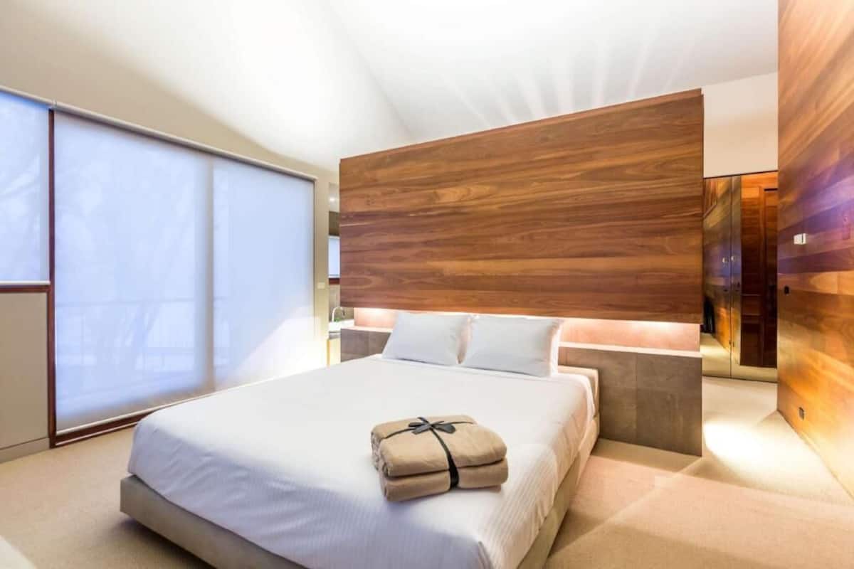 A modern hotel room with a large bed, wooden headboard, and a view of the city.