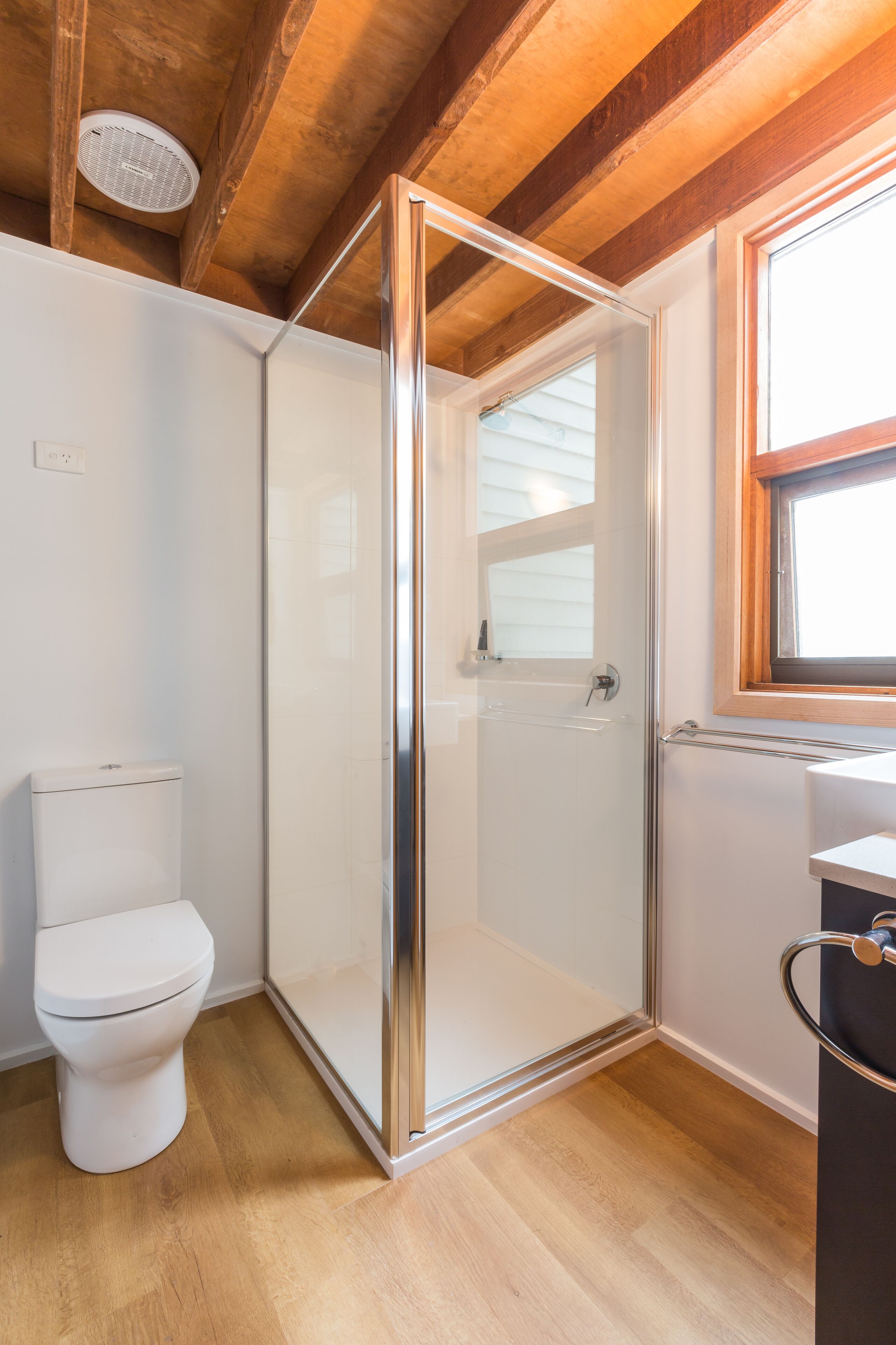 A bathroom with a glass shower enclosure, a white toilet, and a window providing natural light.