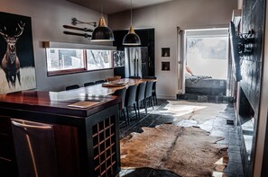 A modern kitchen with a central island, black pendant lights, and a large window.