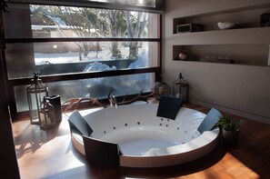 A modern bathroom with a freestanding bathtub, a large window with a view of a snowy landscape, and shelves with decorative items.