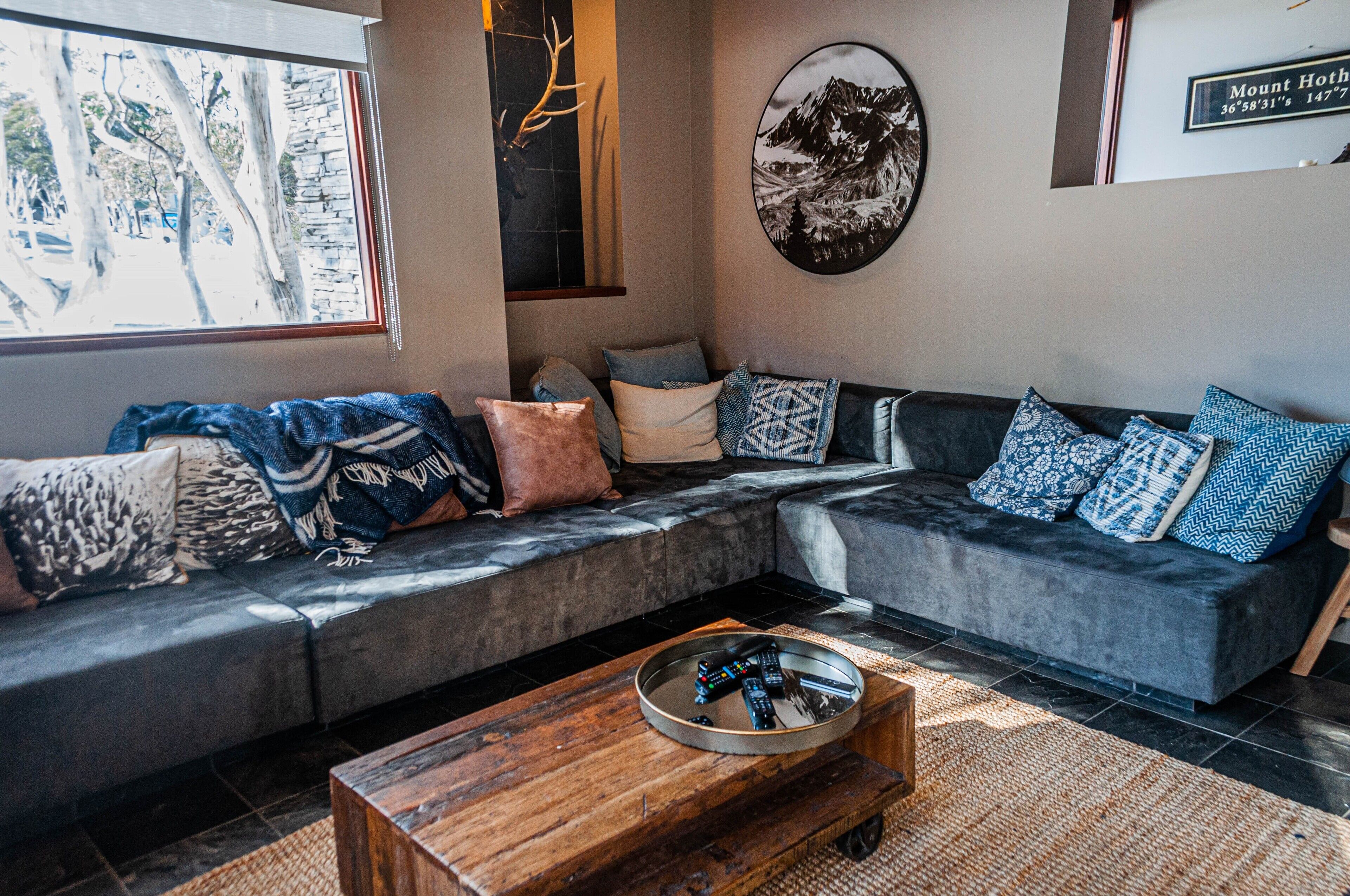 A modern living room with a grey sectional sofa, a wooden coffee table, and a large window with a view of trees.