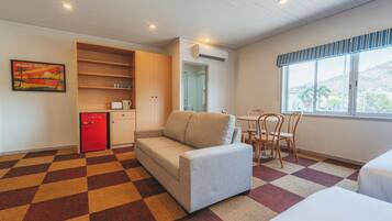 A hotel room with a sofa, a dining table with chairs, a kitchenette, and a window with a view.