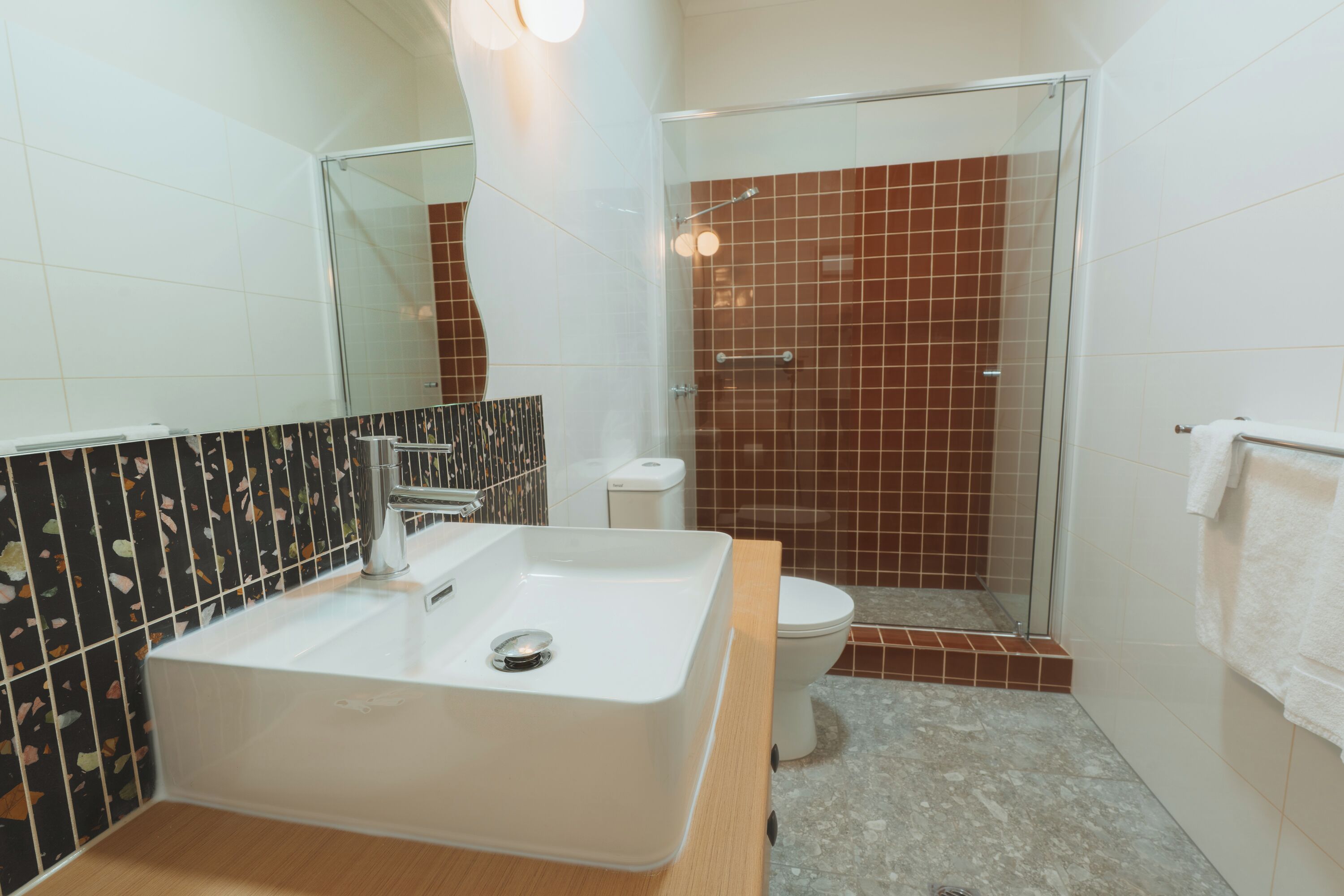 Un baño moderno con un lavamanos grande y blanco, una cabina de ducha con mampara de vidrio y un inodoro.
