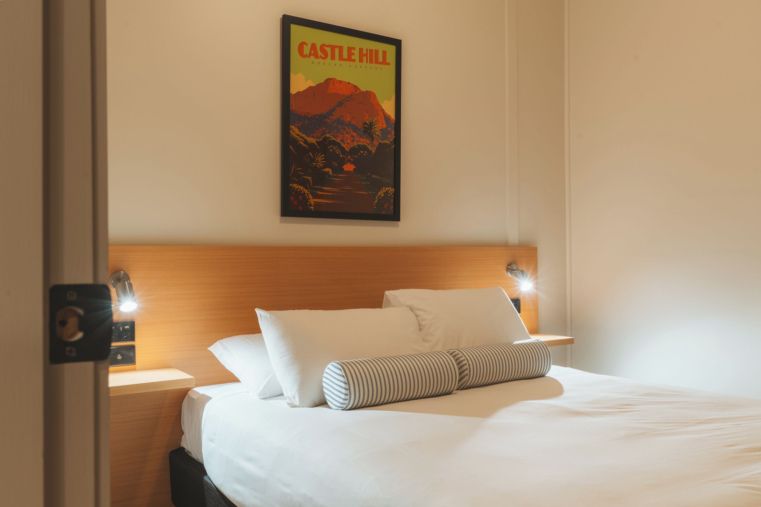 A hotel room with a neatly made bed, a poster on the wall, and a wooden headboard.
