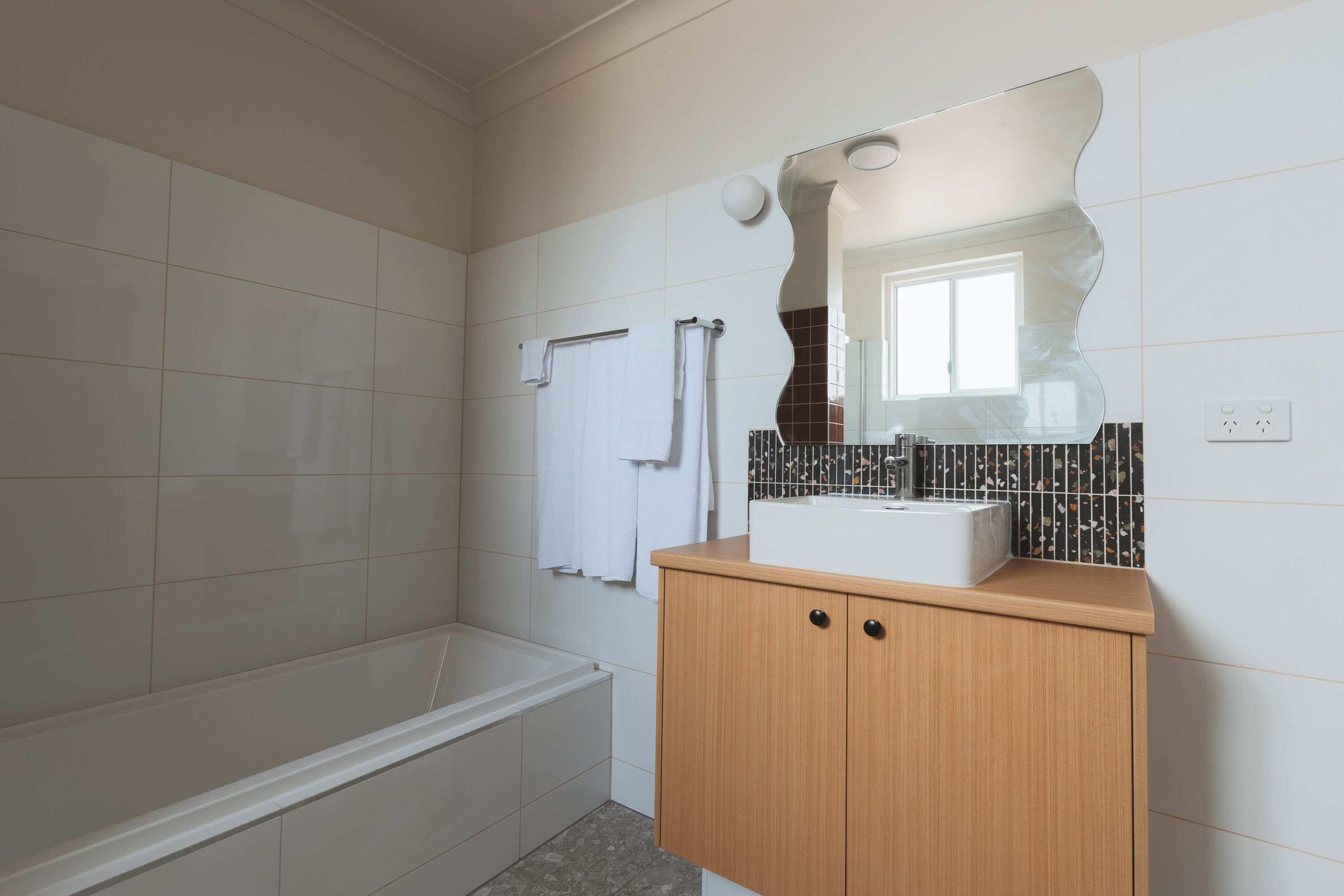 Een badkamer met een bad, een houten wastafelmeubel en een spiegel.