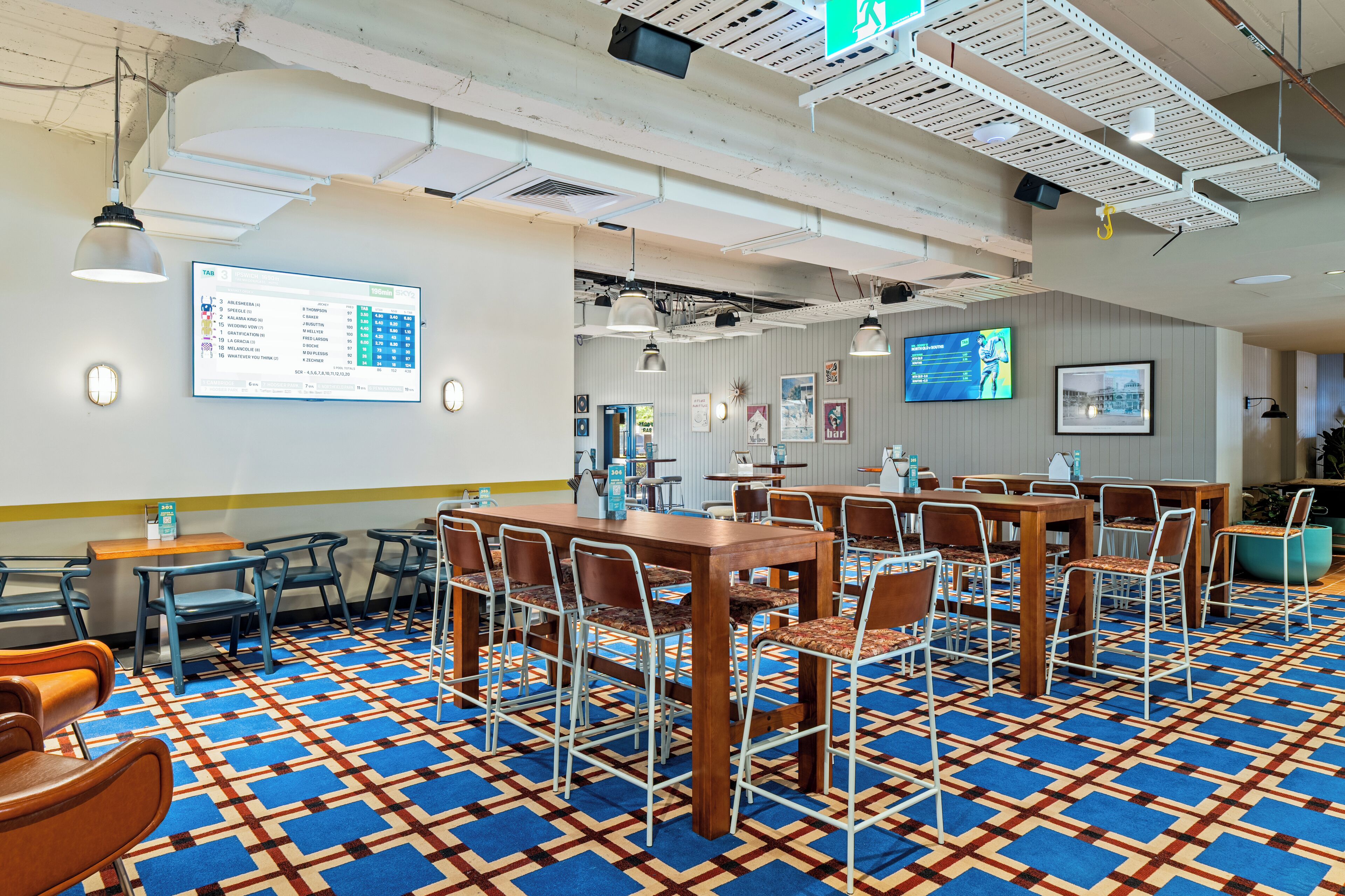 A spacious room with a patterned carpet, multiple tables and chairs, and a digital display on the wall.