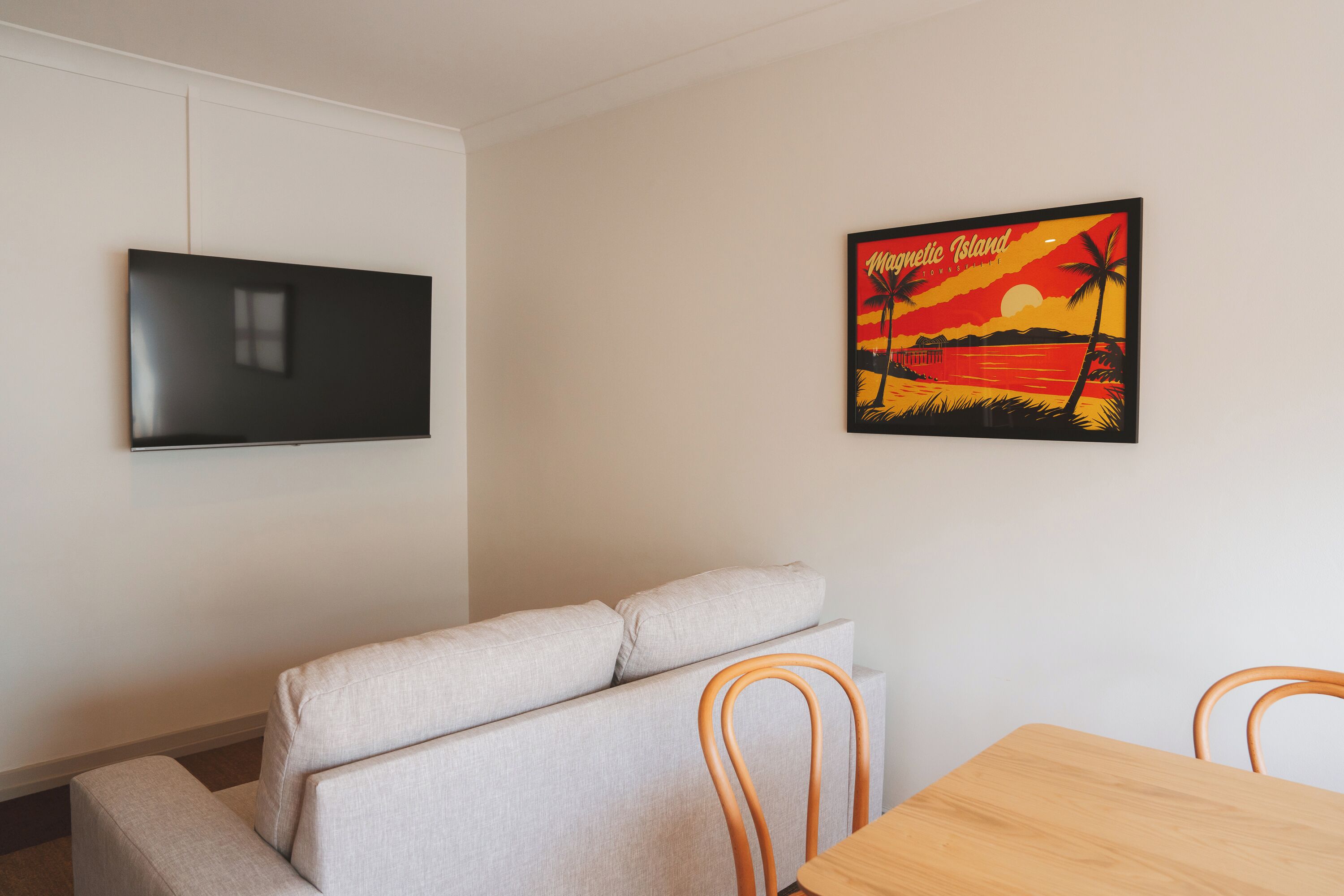 A modern living room with a flat-screen TV, a sofa, and a wooden dining table.