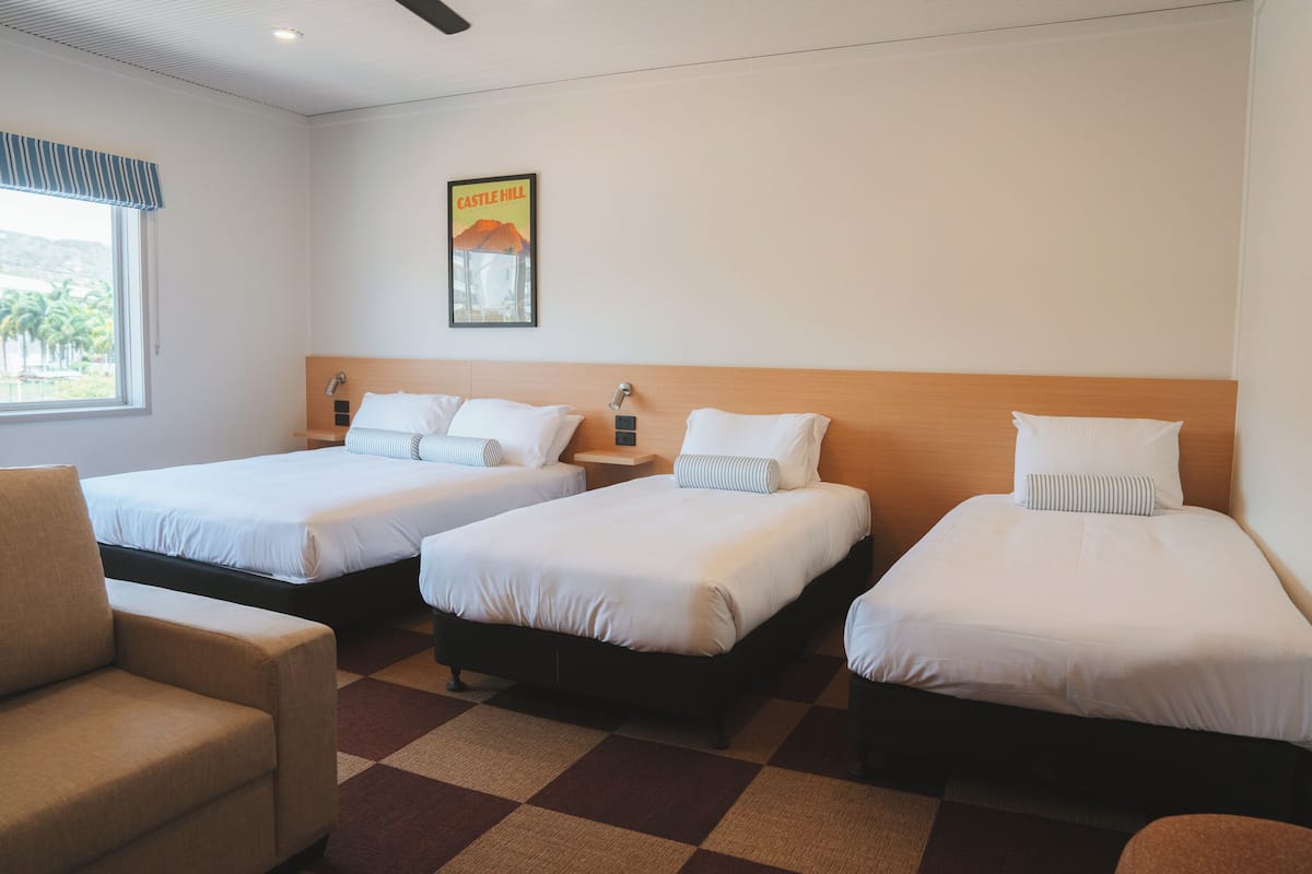 A hotel room with three beds, a sofa, and a window with a view of palm trees.