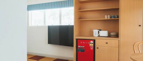 A compact kitchen with a red mini-fridge, wooden cabinets, and a window with a striped valance.