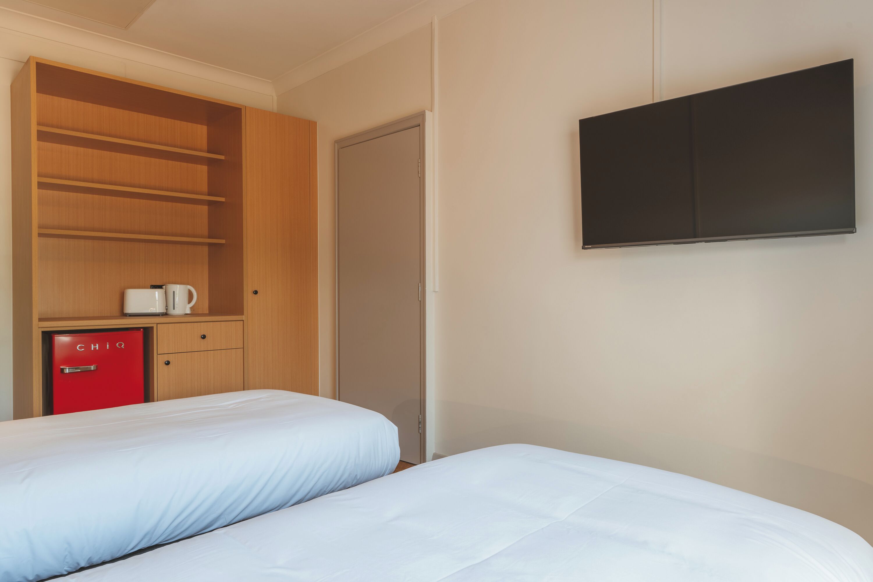 A hotel room with two beds, a wardrobe, a minibar, and a flat-screen TV.