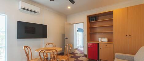 Une chambre moderne équipée d’une table à manger, de chaises, d’un mini-réfrigérateur rouge, d’une télévision et d’un ventilateur de plafond.