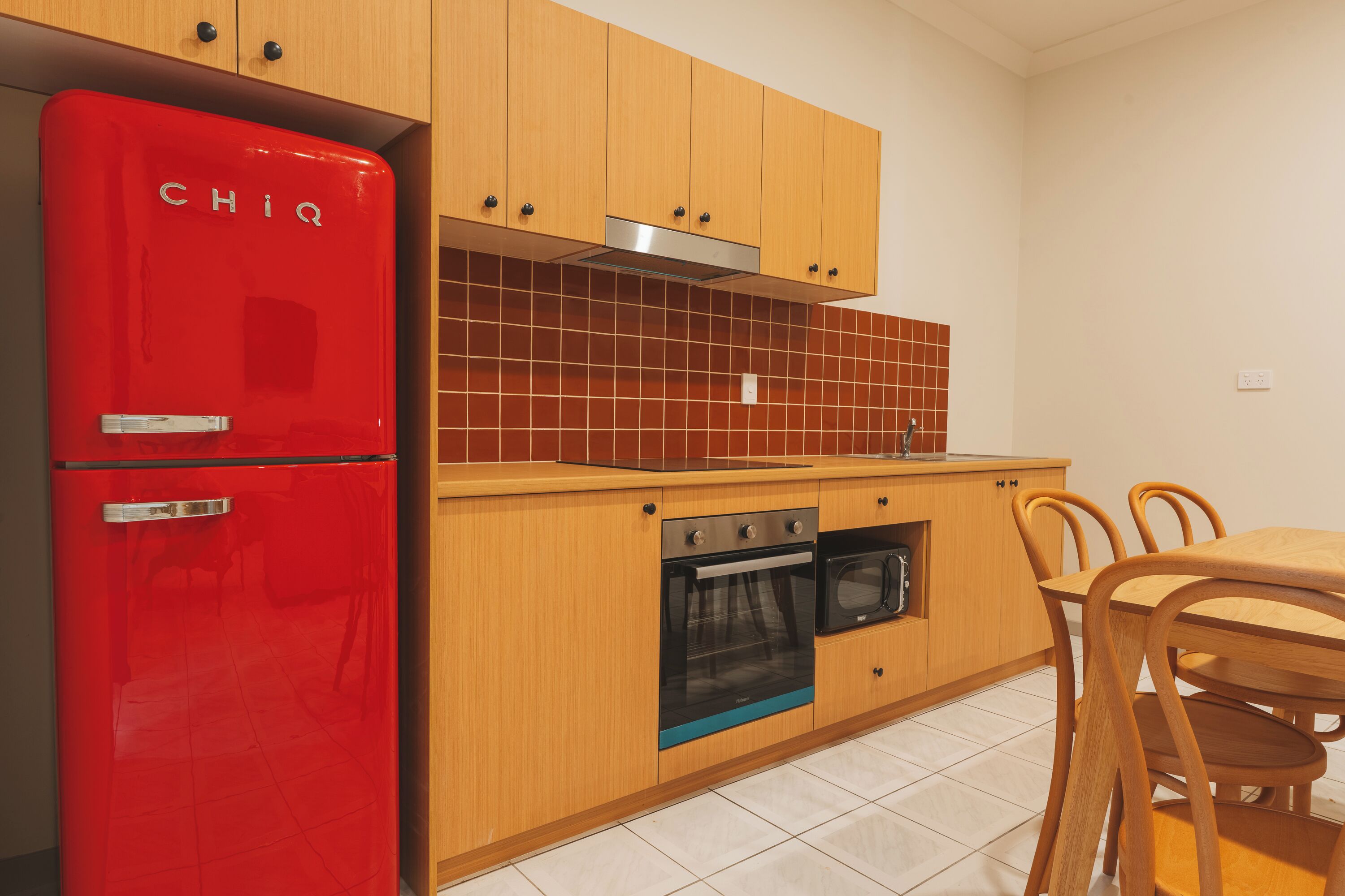 A kitchen with wooden cabinets, a red refrigerator, a stove, and a dining table with chairs.