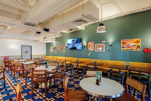 Un ristorante con sedute a cabina, tavoli e sedie, uno schermo televisivo e diverse decorazioni alle pareti.