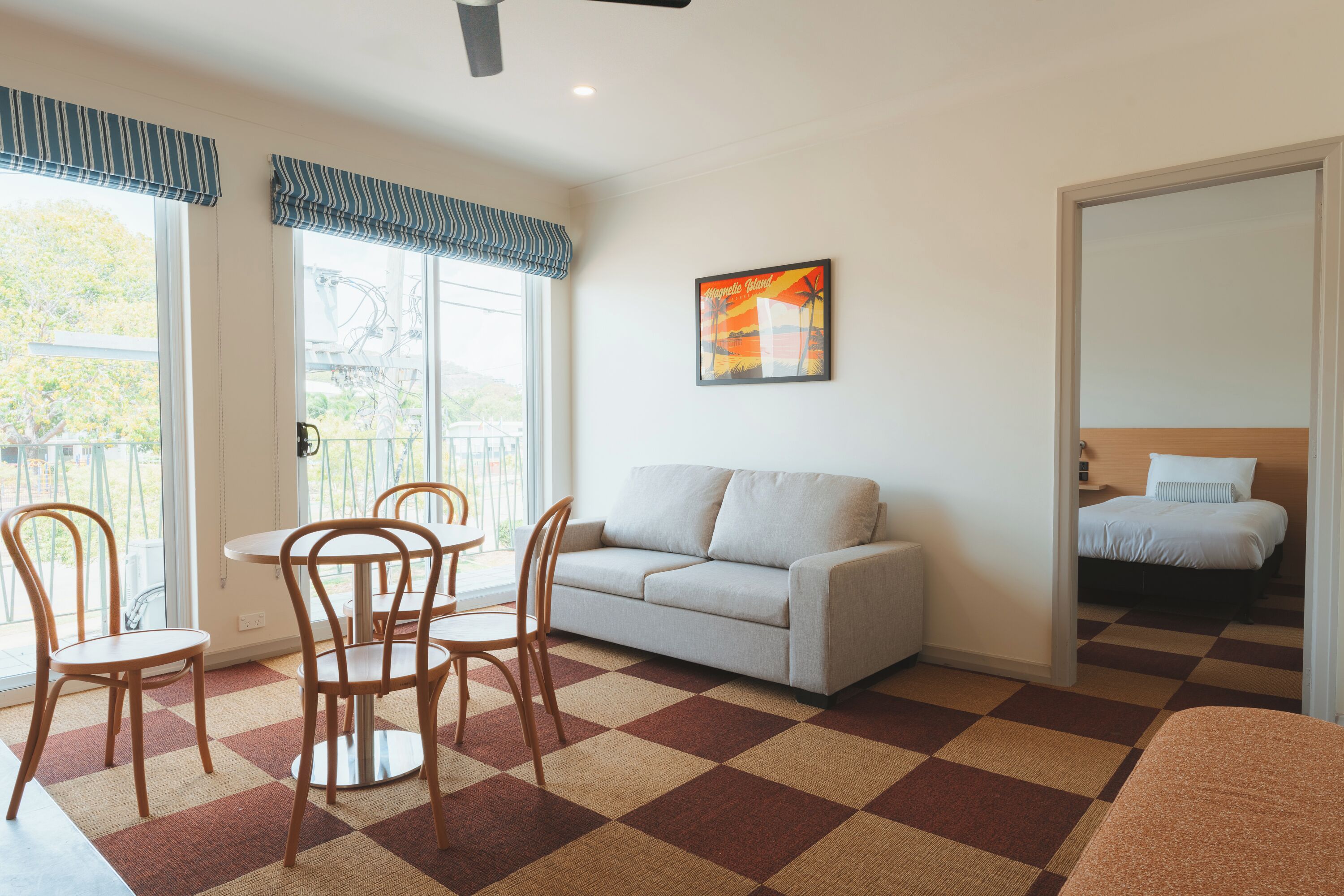 A room with a checkered carpet, a sofa, a dining table with chairs, and a bed.