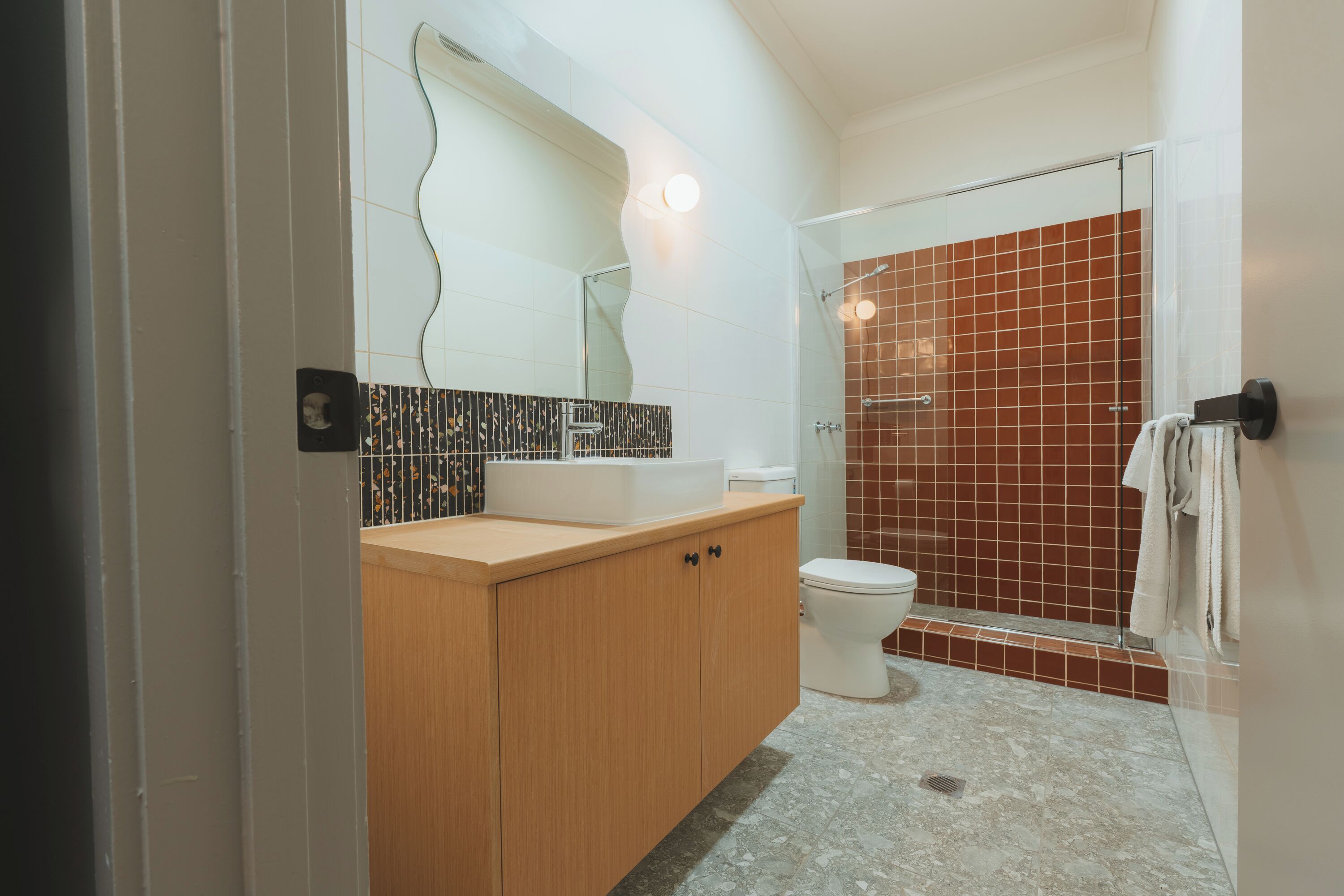 A modern bathroom with a wooden vanity, a white sink, a toilet, and a glass shower enclosure.